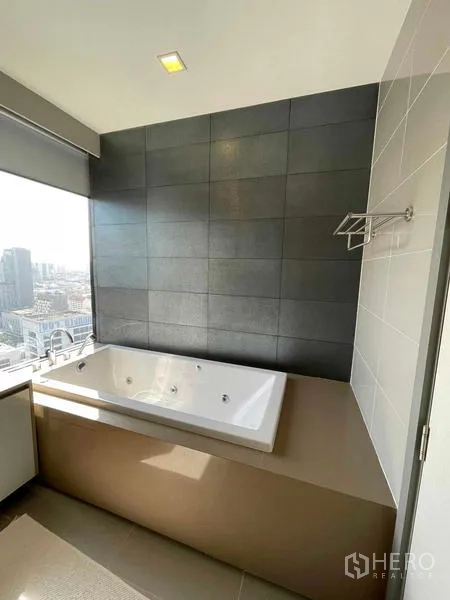 คอนโด ให้เช่าหรือขายในBang Rak, Bangkok - ภาพใกล้อ่างอาบน้ำบิวท์อินติดผนังกระเบื้องสีเข้ม มีหน้าต่างมองเห็นวิวเมือง