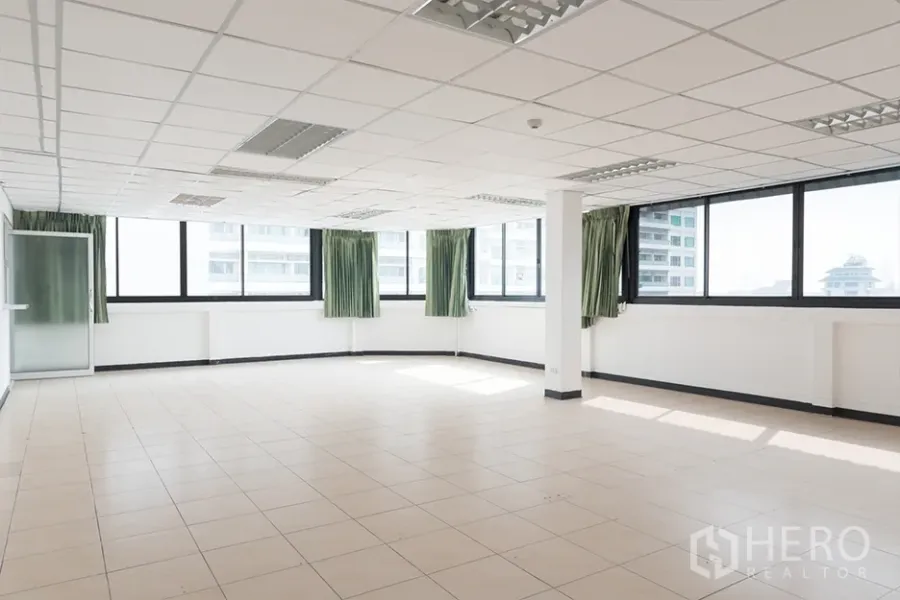 办公空间 出租在Watthana, Bangkok - 明亮的空置办公空间，瓷砖地面、吊顶灯具，转角大窗配绿色窗帘，可观城市景致。