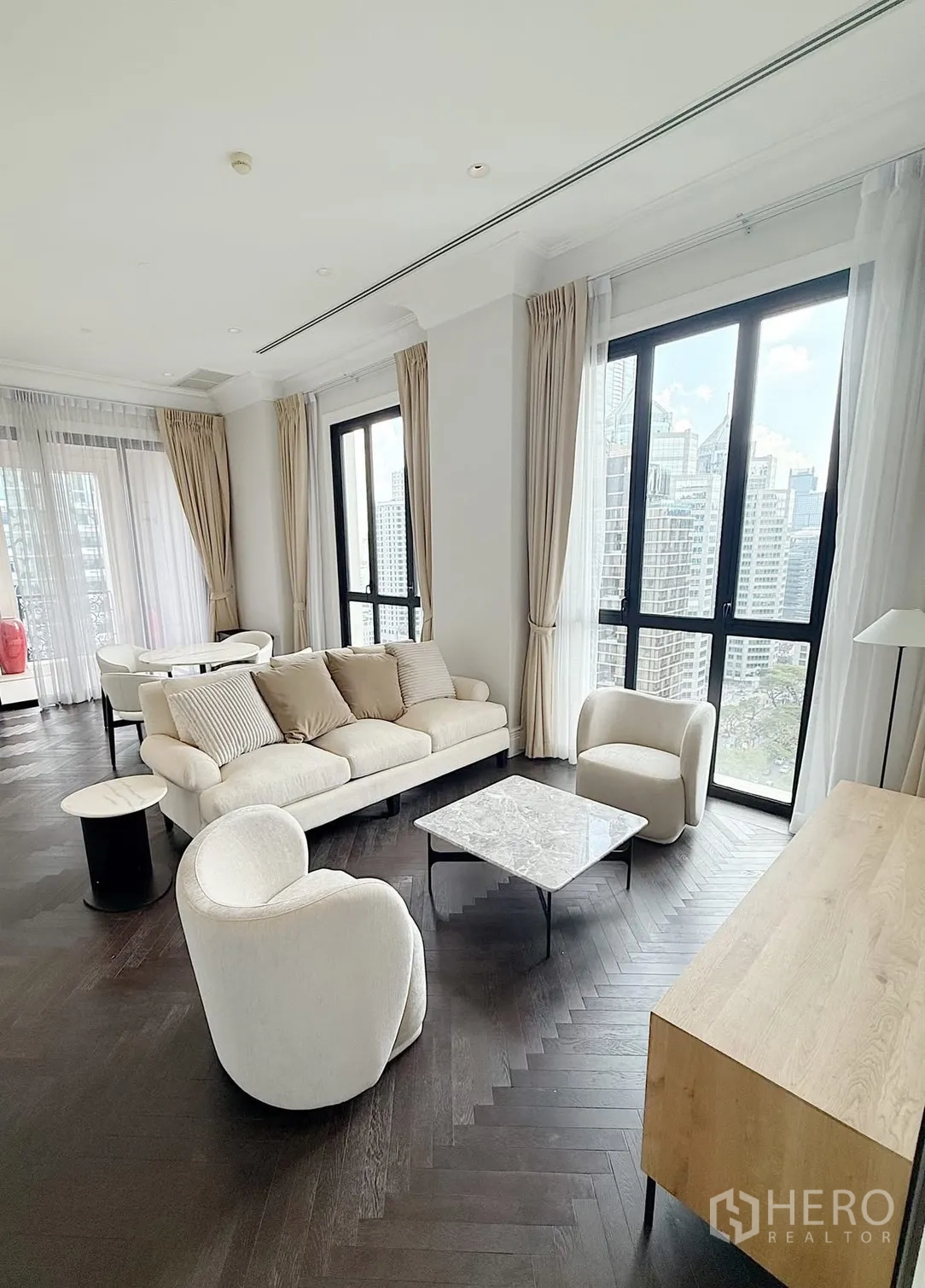 公寓 for rent or sale in Pathum Wan, Bangkok - 明亮客厅，浅色家具、人字形木地板与全景城市景观。