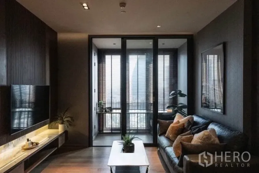 公寓 出租在Khlong Toei, Bangkok - 深色调客厅，木质电视墙、皮沙发与通向日光房的玻璃滑门。