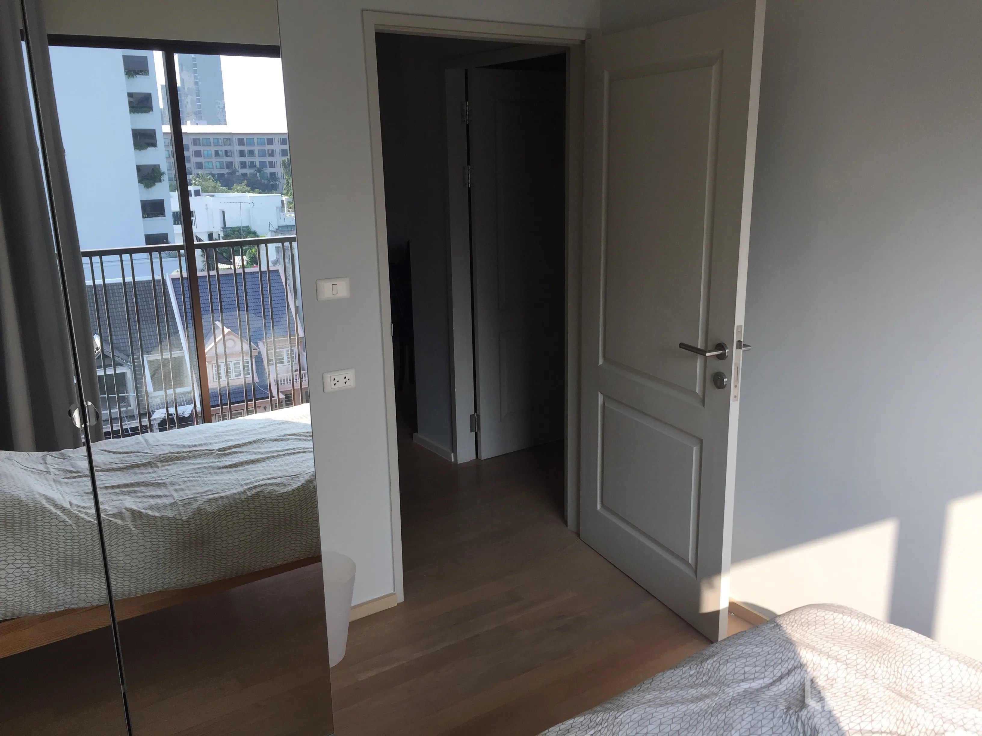 คอนโด ให้เช่าในBangkok - ห้องนอนพื้นไม้ สีอ่อน ประตูเปิดสู่โถงทางเดิน และหน้าต่างใหญ่ติดระเบียง