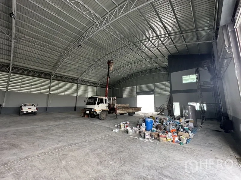 Factory for rent in Pathum Thani - Industrial hall with equipment and materials near mezzanine office and shutter door.