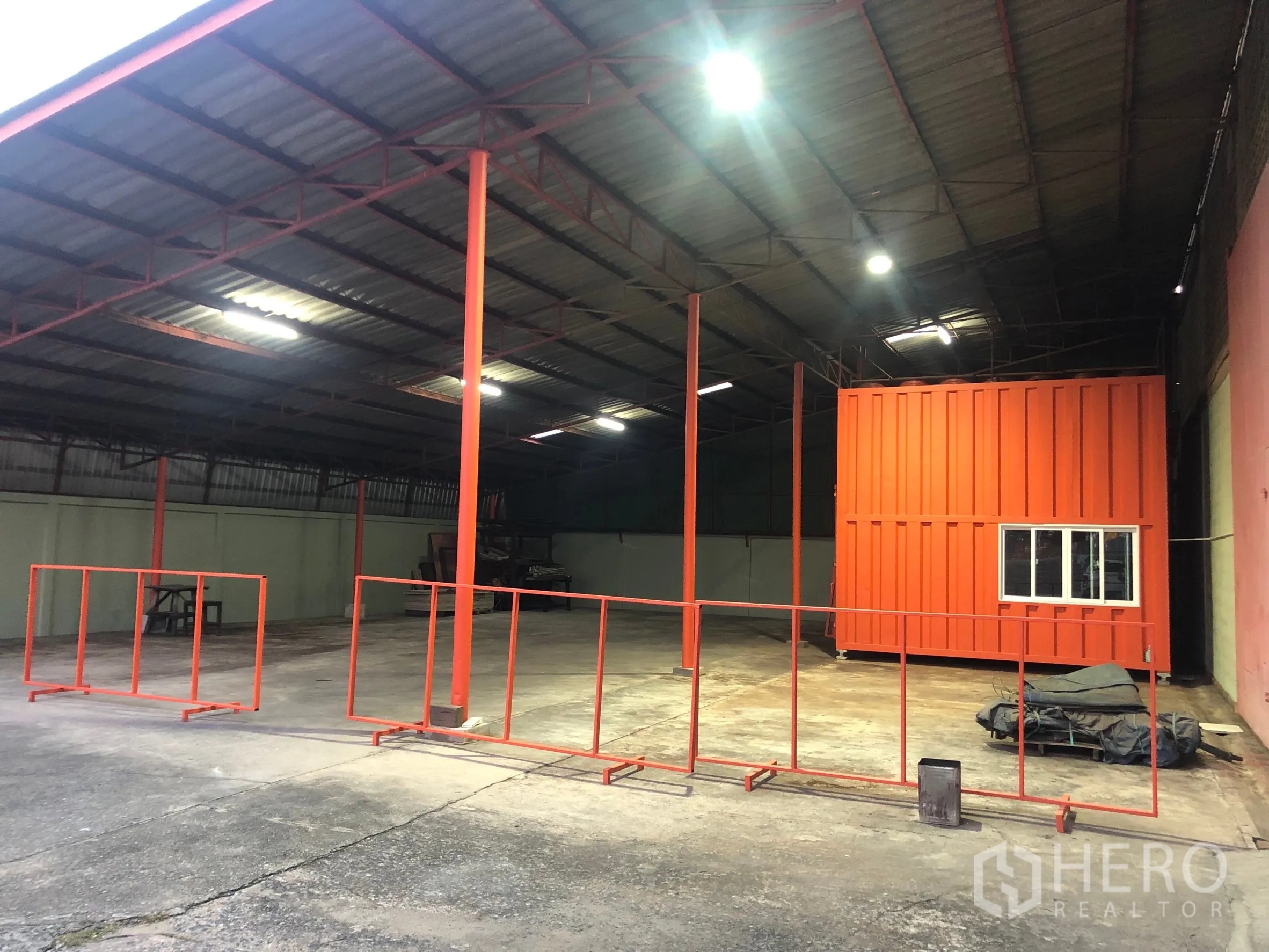 Warehouse for rent in Min Buri, Bangkok - Open-sided warehouse bay with steel roof, overhead lighting and orange safety rails beside the modular office.