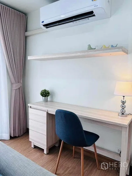 Condominium for rent in Watthana, Bangkok - Compact home office corner with wooden desk, shelf, lamp and air conditioner.