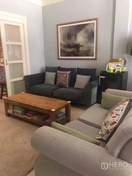 ทาวน์เฮาส์ ให้เช่าหรือขายในBangkok - ห้องนั่งเล่นอบอุ่น โซฟาสีเทา โต๊ะกลางไม้ และประตูบานเลื่อนในทาวน์เฮ้าส์