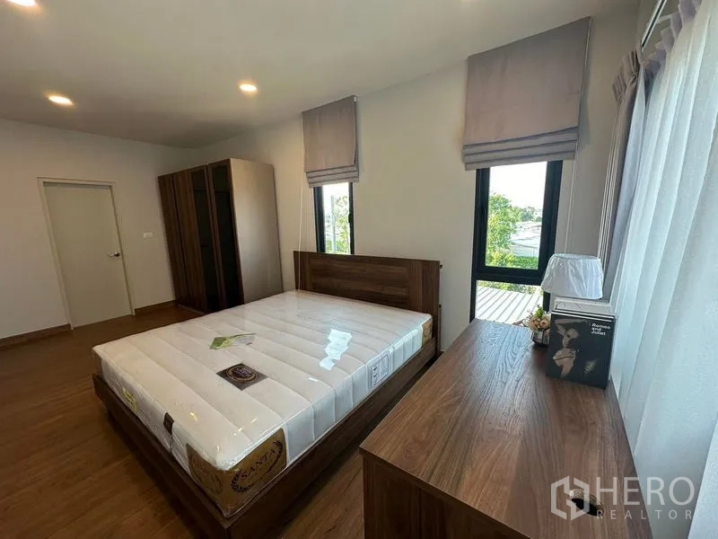 Detached House for rent in Bang Phli, Samut Prakan - Secondary bedroom with wood bedframe, desk, wardrobe and corner windows.