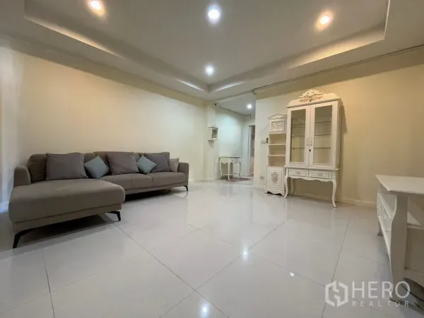 Townhouse for rent in Phaya Thai, Bangkok - Bright lounge featuring sectional sofa, white display cabinet and tiled floors with downlights.