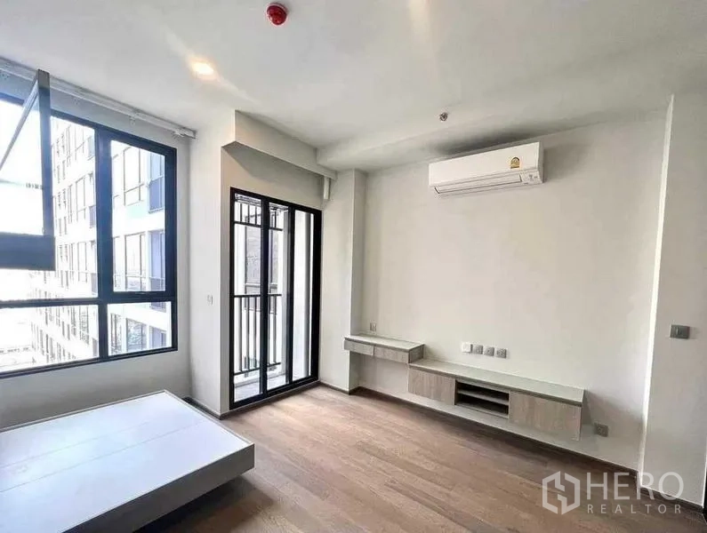 Condominium for sale - Living area with sliding balcony door, wall-mounted TV console, air conditioner and wood flooring.