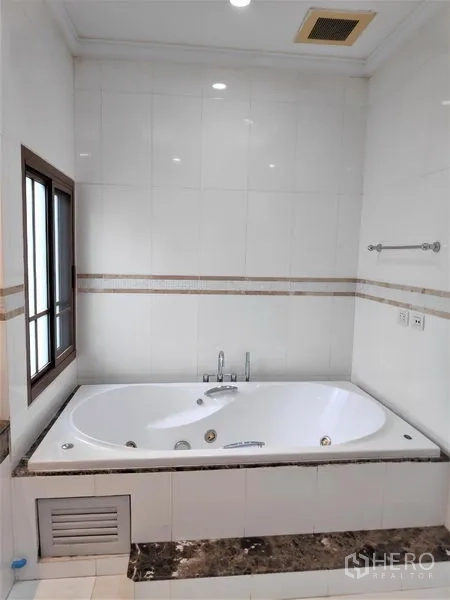 独立式住宅 出租在Watthana, Bangkok - 白色瓷砖浴室，设有大尺寸按摩浴缸，靠窗而置。