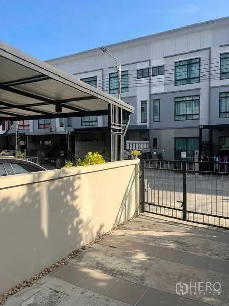 ทาวน์เฮาส์ ให้เช่าในSuan Luang, Bangkok - ลานหน้าบ้านพร้อมรั้วหน้าทาวน์เฮ้าส์ มองเห็นแถวทาวน์โฮมและที่จอดรถมีหลังคา