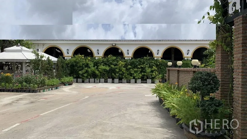Warehouse for rent in Phra Pradaeng, Samut Prakan - Arched colonnade facade and hedge-lined walkway beside an open yard.