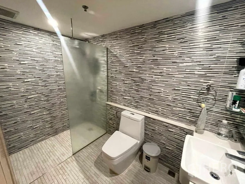 Condominium for rent in Sathon, Bangkok - Modern bathroom with mosaic tile walls, glass walk-in shower, toilet and compact vanity basin.