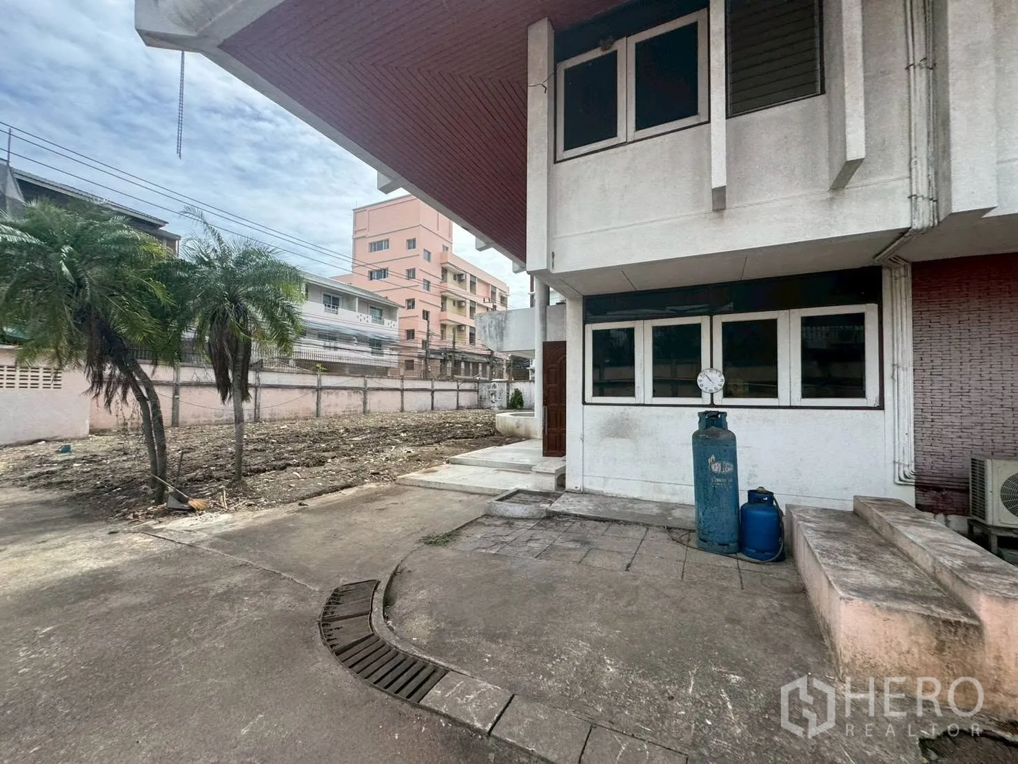 Detached House for rent or sale in Watthana, Bangkok - Side yard with cleared soil area and two palm trees by the wall.