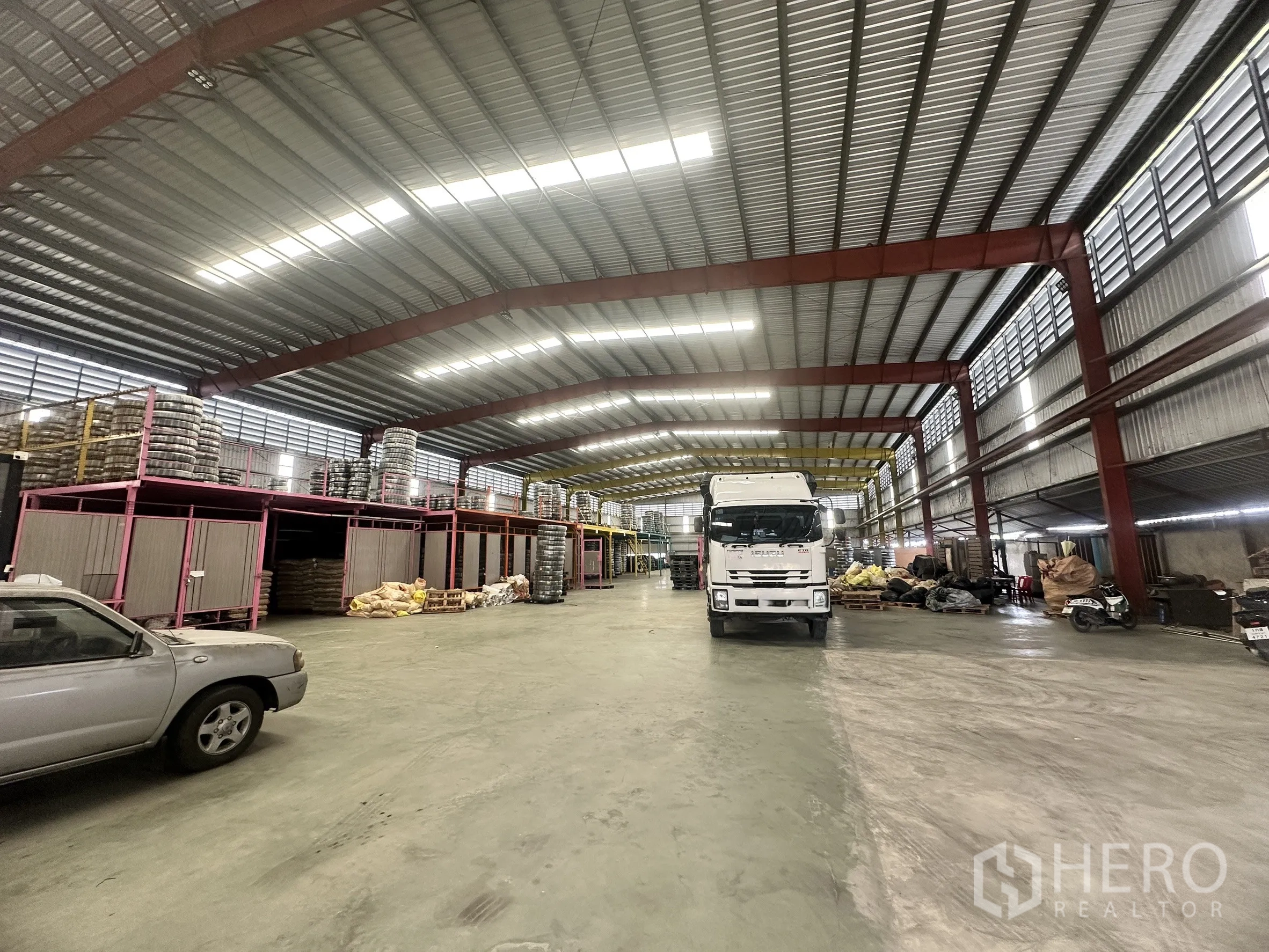 Warehouse for rent in Mueang Samut Prakan, Samut Prakan - Open warehouse floor with truck access, mezzanine storage racks and bright roof lighting.