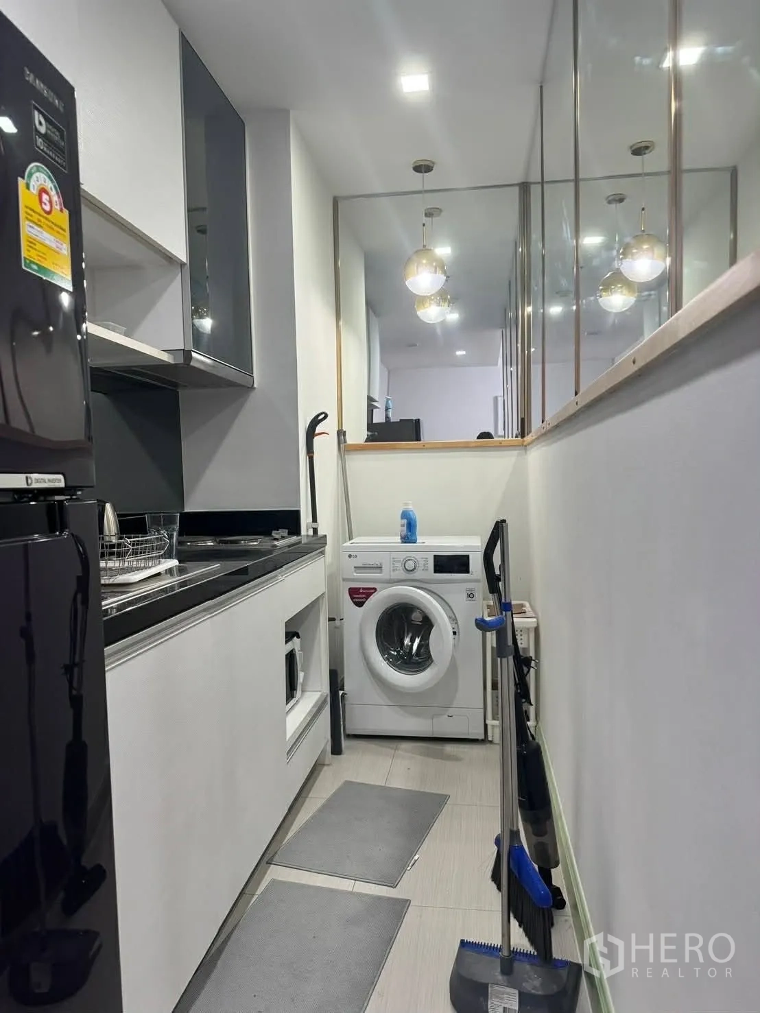 Condominium for rent in Watthana, Bangkok - Kitchen corridor with mirrored wall, worktop, and front-load washing machine.
