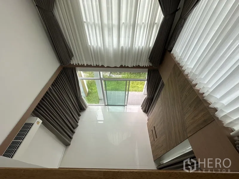 บ้าน ขายในLam Luk Ka, Pathum Thani - มุมมองจากชั้นลอยลงสู่ห้องนั่งเล่นเพดานสูงและสวน