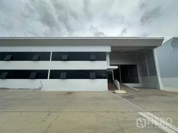 工厂 出租在Wang Noi, Phra Nakhon Si Ayutthaya - 现代化工厂立面，黑色带状窗、带顶装卸区与宽阔混凝土场地。