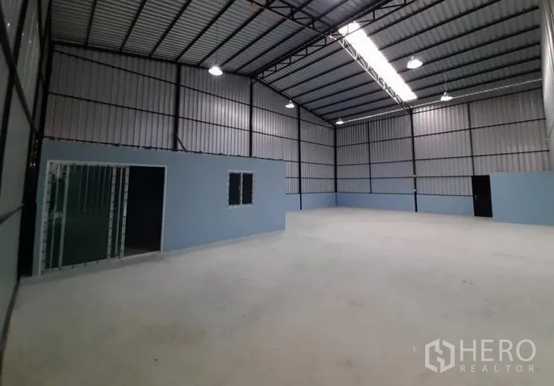 Warehouse for rent in Lam Luk Ka, Pathum Thani - Open storage area showing the office block, skylight strip and high‑bay lamps under a steel truss roof.