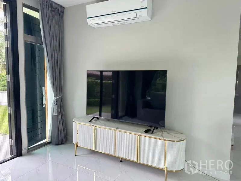 Detached House for rent in Bang Phli, Samut Prakan - Media corner with a large flat-screen TV on a marble console, split air-conditioner and curtains.