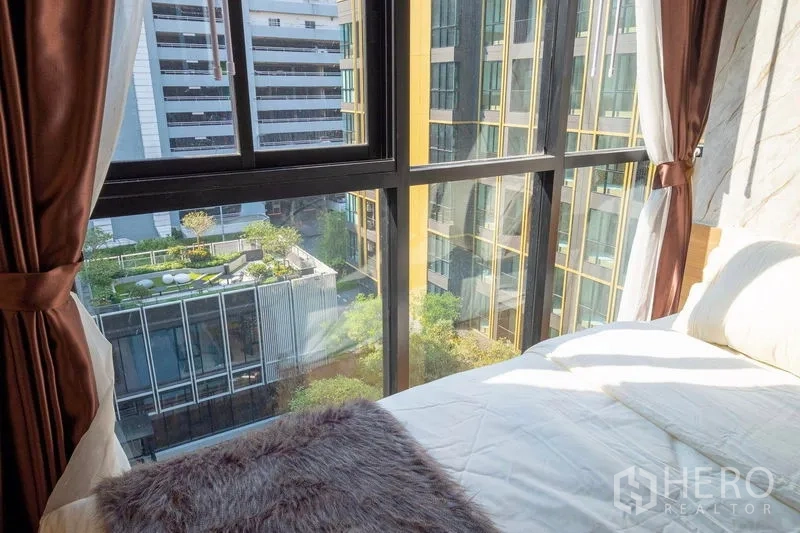 คอนโด ให้เช่าในBang Na, Bangkok - มุมห้องนอนพร้อมหน้าต่างเต็มบาน มองเห็นสวนส่วนกลางและอาคารโมเดิร์น