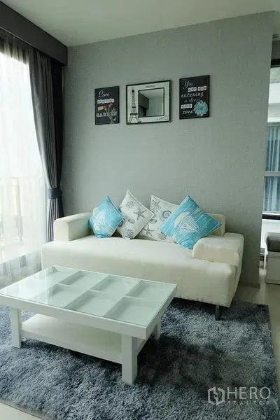 公寓 出租在Khlong Toei, Bangkok - 明亮客厅，白色沙发与玻璃茶几，大窗配窗帘。