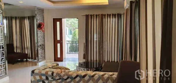 บ้าน ขายในKhan Na Yao, Bangkok - ห้องนั่งเล่นสว่างมีโซฟาลายกราฟิก ม่านลายทาง และประตูออกสู่เฉลียงหน้าบ้าน