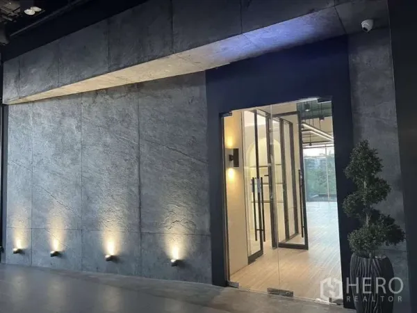 零售空间 出租 - 混凝土质感外墙上的玻璃门店入口，配壁洗灯照明。