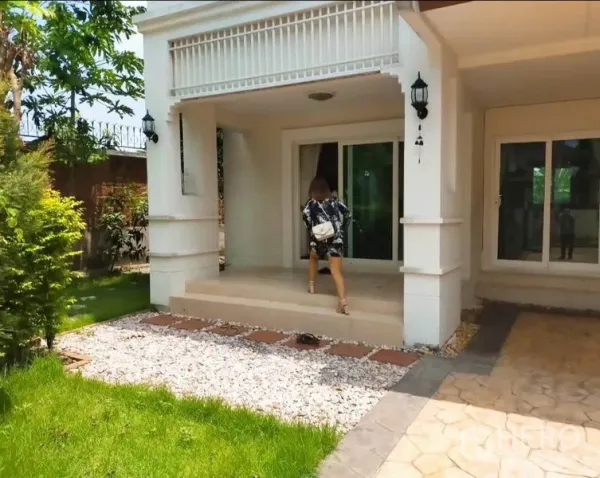 บ้าน ให้เช่าหรือขายในBang Yai, Nonthaburi - เฉลียงหน้าบ้านแบบมีหลังคา พร้อมบันได โคมไฟผนัง และประตูกระจกบานเลื่อน มองสู่สนามหญ้า