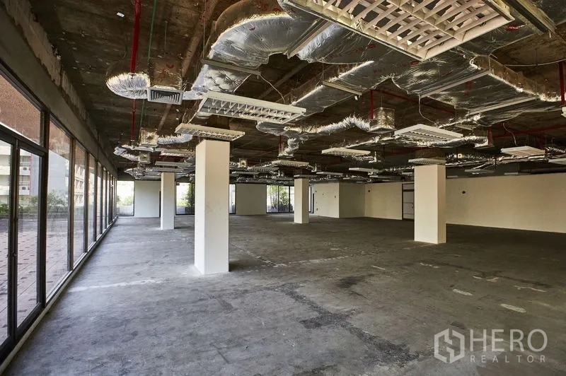 办公空间 出租在Bangkok - 开放式毛坯办公区，外露吊顶管线与多根立柱，整面落地窗。