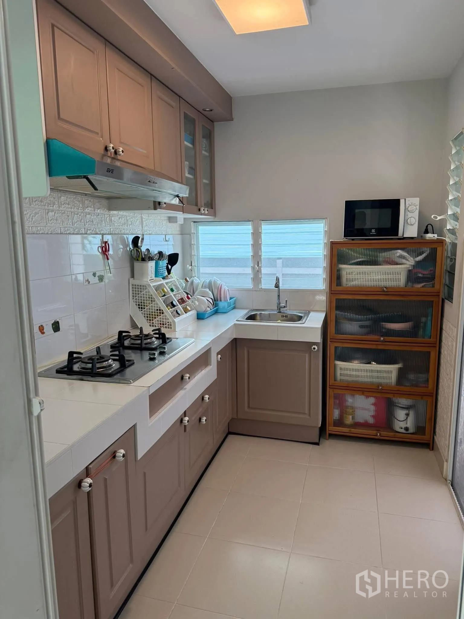 Townhouse for rent or sale in Sai Mai, Bangkok - Compact L-shaped kitchen with gas hob, upper cabinets and a windowed sink.