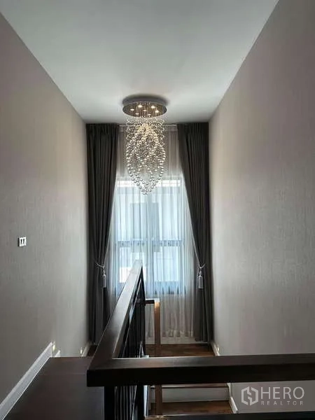 独立式住宅 出售在Prawet, Bangkok - 楼梯平台，挑高窗帘与水晶吊灯。