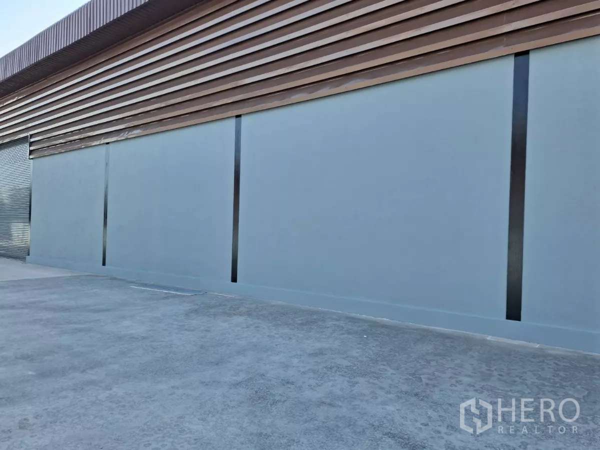 工厂 出租在Mueang Samut Sakhon, Samut Sakhon - 仓库侧立面，金属墙面与卷帘门，铺装装卸区域。