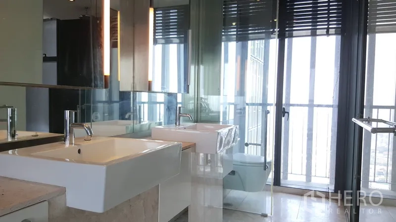 Condominium for rent in Sathon, Bangkok - Contemporary bathroom with double sinks, glass-enclosed shower, and tall windows.
