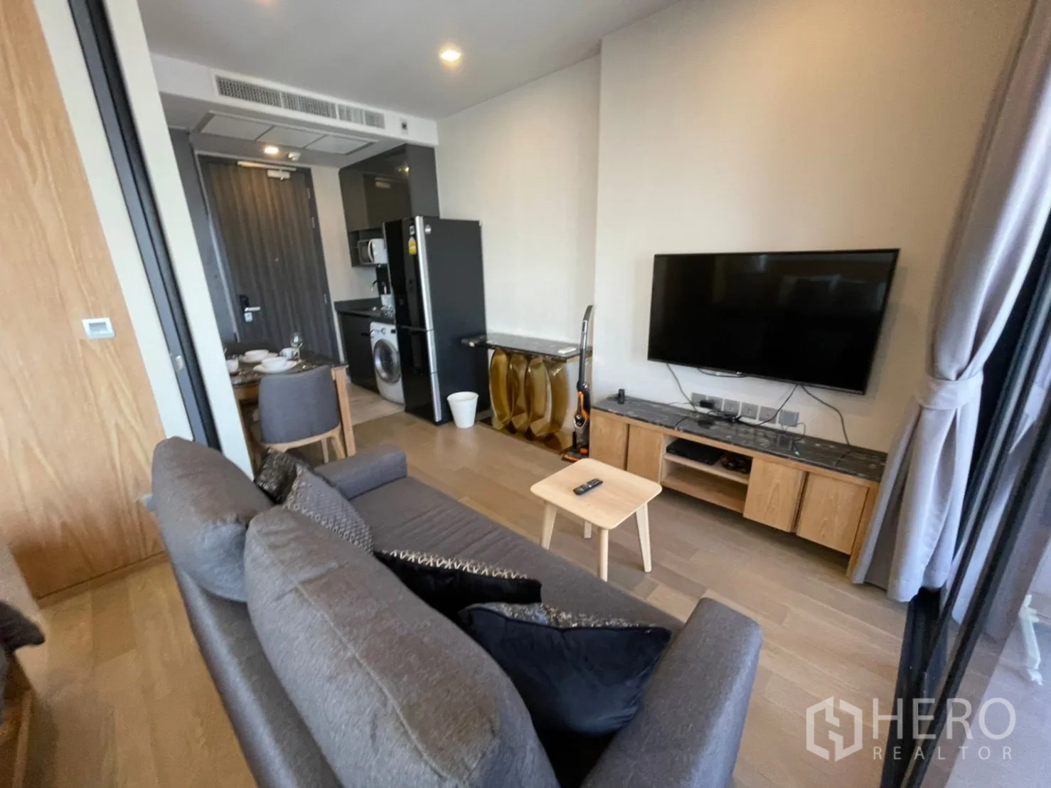 公寓 for rent in Watthana, Bangkok - 起居区配壁挂电视、灰色沙发，入口旁为厨房。