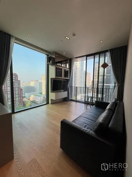 Condominium for rent - Living room with black leather sofa, TV wall unit, and corner floor-to-ceiling windows overlooking the city.