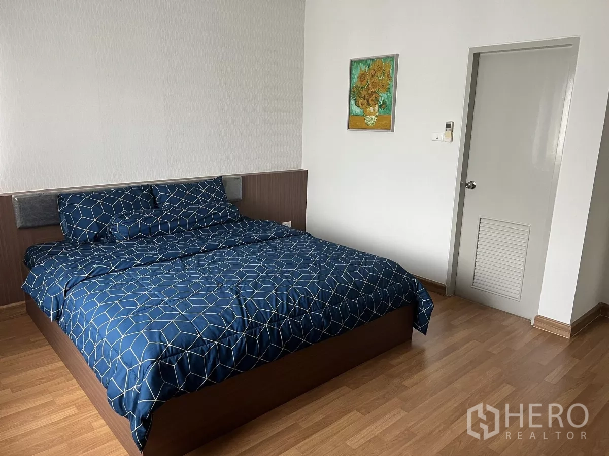 Detached House for rent or sale in Don Mueang, Bangkok - Cozy bedroom with king bed, wood floor, white door and framed artwork.
