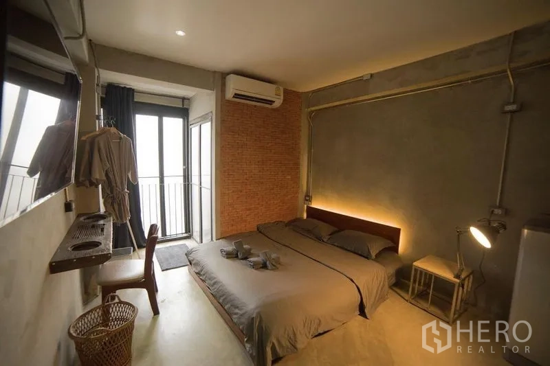 店屋 出租或出售在Din Daeng, Bangkok - 工业风卧室，裸露混凝土与砖墙，暖色床头灯光，带小阳台。