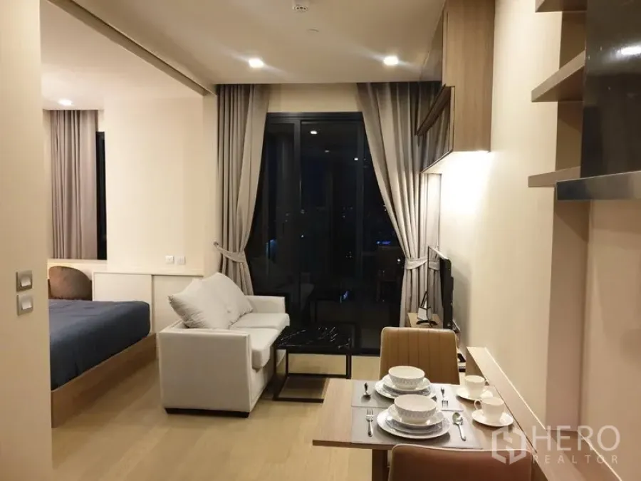 Condominium for rent in Watthana, Bangkok - Open-plan living area with sofa, TV and balcony doors, bedroom partition on the left, night city view.