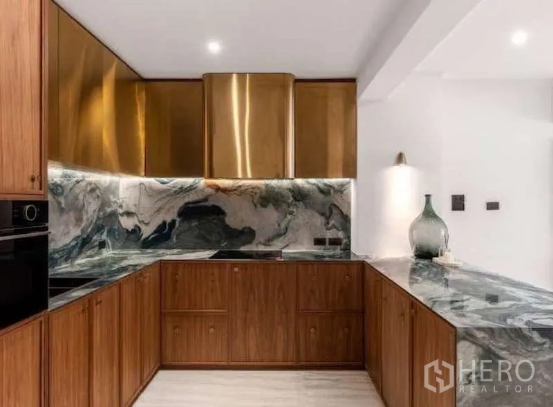 Townhouse for sale in Sathon, Bangkok - Close-up of L-shaped kitchen with stone counters, brass hood and built-in oven.