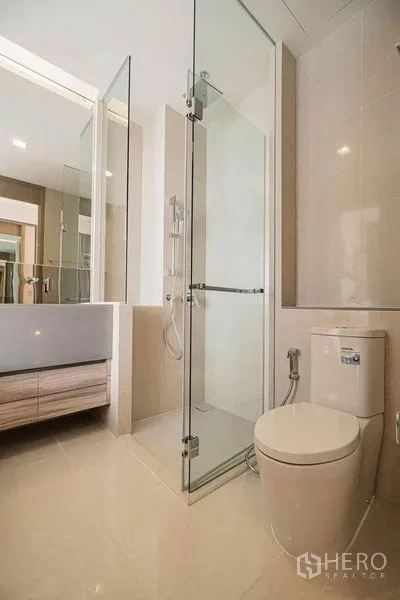 Condominium for rent in Watthana, Bangkok - Clean bathroom with glass-enclosed shower, modern toilet and light tile finishes.