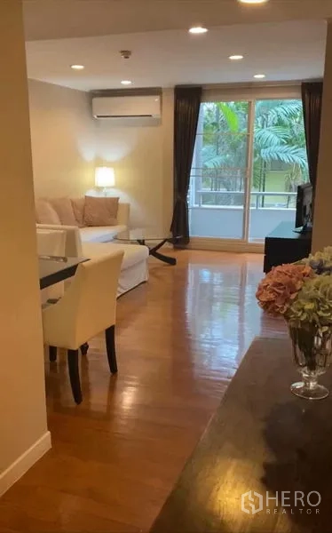 Condominium for rent in Pathum Wan, Bangkok - Open-plan living and dining area with air conditioner and balcony access, wood floors.