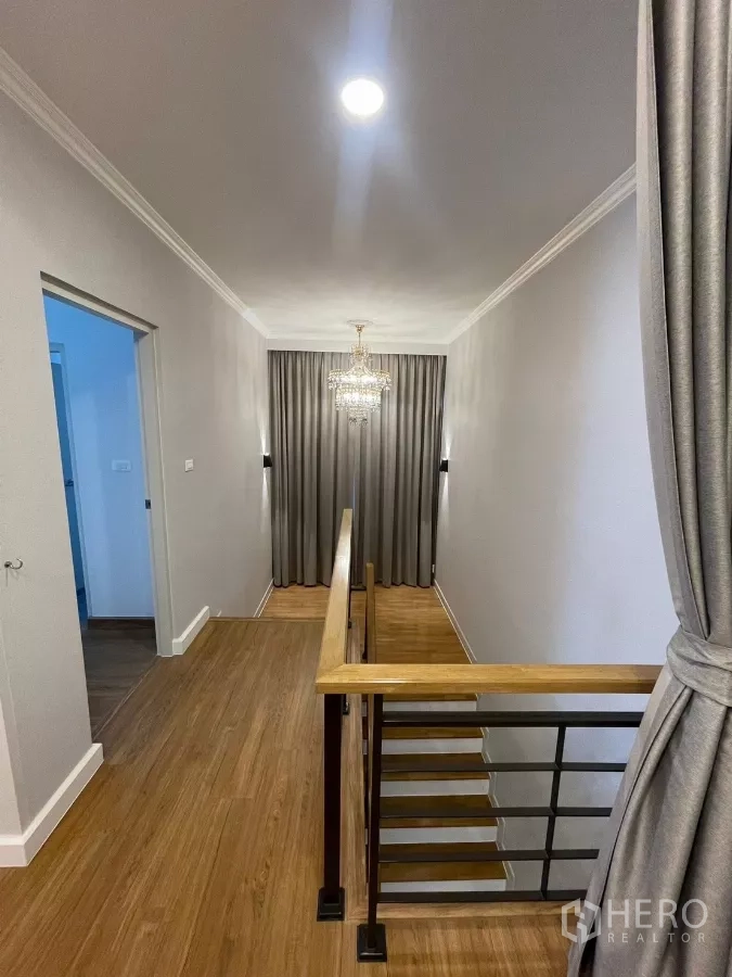 独立式住宅 出租在Bang Phli, Samut Prakan - 二层走廊，木地板、栏杆与水晶灯。