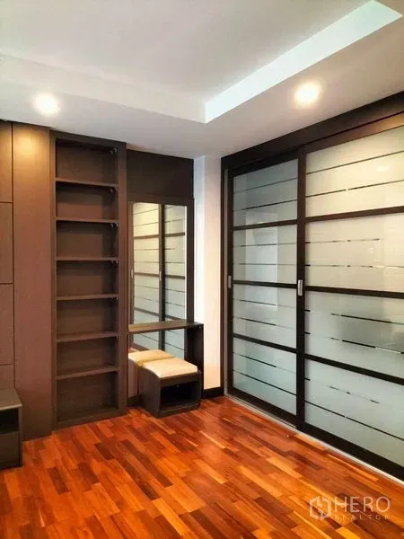 Condominium for rent in Watthana, Bangkok - Built-in shelving and vanity beside frosted glass sliding doors on rich wooden flooring.