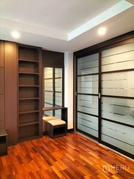 Condominium for rent in Watthana, Bangkok - Built-in shelving and vanity beside frosted glass sliding doors on rich wooden flooring.