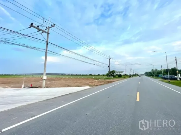 Land for sale in Lam Luk Ka, Pathum Thani - Wide two-lane road with power lines and a paved entrance beside cleared land in Lam Luk Ka.