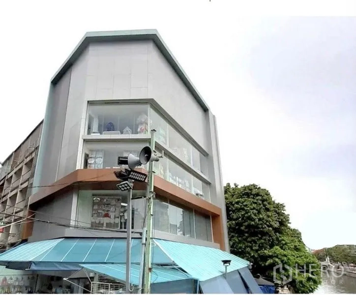 店屋 出租在Pathum Wan, Bangkok - 现代转角商铺外观，整面落地玻璃与蓝色雨棚，位于曼谷。