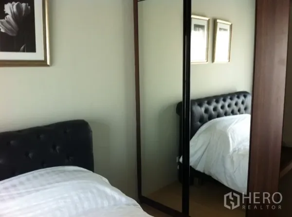 คอนโด ให้เช่าในBangkok - มุมห้องนอนพร้อมหัวเตียงบุผ้าทรงปุ่ม ตู้เสื้อผ้าบานกระจก และโทนสีอบอุ่น