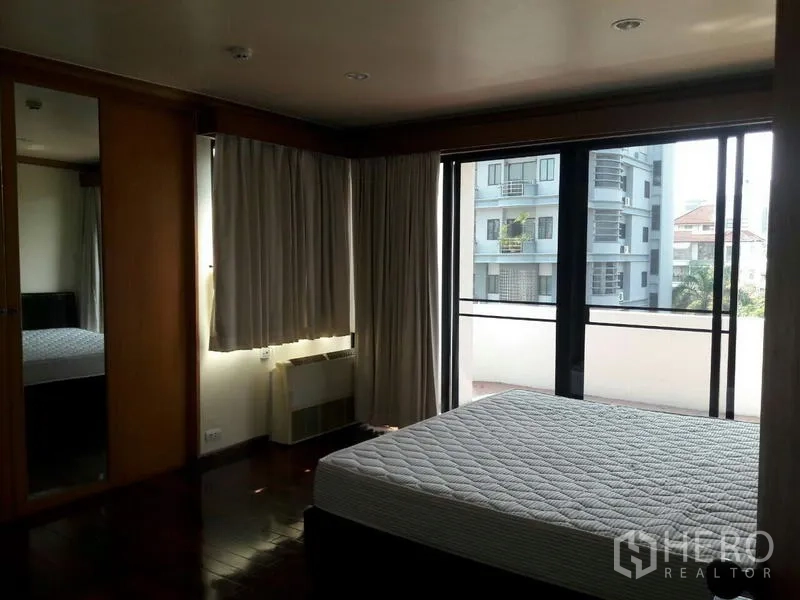 Condominium for rent in Pathum Wan, Bangkok - Bright bedroom with wood floors, mirrored wardrobe, and sliding doors opening to a balcony.