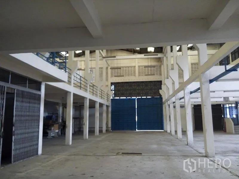 Warehouse for rent in Min Buri, Bangkok - Open warehouse floor facing large blue loading doors and mezzanine walkways.