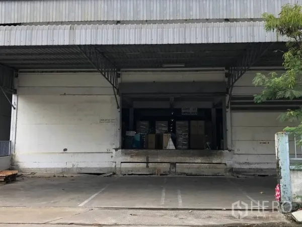 Warehouse for rent in Bang Bo, Samut Prakan - Raised loading bay with roll-up doors and stacked pallets beneath a steel canopy.